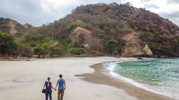 一对夫妇在田园诗般的科卡海滩上散步 印度尼西亚弗洛雷斯隐藏的宝石 情侣们正在享受他们浪漫的逃离 波浪轻柔地冲刷着海岸 后面有小山 幸福与爱情 — 图库照片