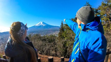 A couple standing on the hilltop above Chureito Pagoda, Japan and pointing at Mt Fuji in the back. They are having a lot of fun, enjoying beautiful landscape. Holly mountain. Clear and sunny day