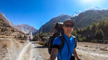 A couple trekking along the barren pathway in Annapurna Circuit in Nepal. They are having fun, enjoying the view. There is a lush green Himalayan valley around. Snow caped mountains in the back.