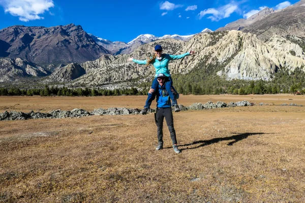 Man holding woman on his shoulders along Annapurna Circuit Trek in Nepal. They are having fun. There is a vast, dried plain around her and high Himalayan chain in the back. Happiness and togetherness