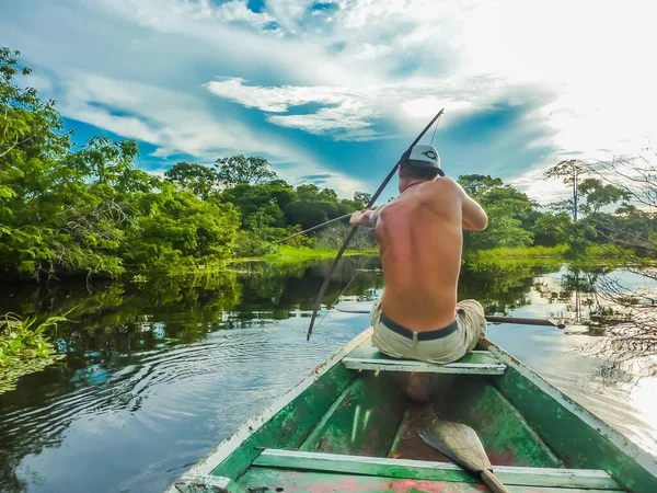 A young man bow hunting for Piranhas, in the middle of the Amazon rain forest in Brazil, from a small local boat.