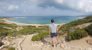 A man wearing a cap enjoying the view on Lara Beach, Cyprus from above. Hidden gem, not spoiled by tourists. Solitude, calm feelings, waves gently spreading on the beach. turquoise color of the water