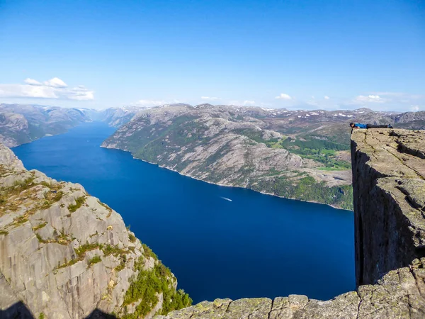 A man wearing blue T-shirt leaning over the edge of a steep cliff of Preikestolen, Pulpit Rock, with a view on Lysefjorden. Man is trying to overcome his fear of height. Overcoming acrophobia