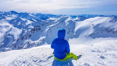 Skiing young man sitting on the snow in Moelltaler Gletscher, Austria, enjoying the view. Lots of snow in the mountains. Endless Alps chain. Winter wonderland, paradise. Calmness and happiness.