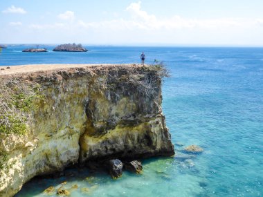 A man in shorts walking at the edge of cliffs of Pink Beach in Lombook, Indonesia. The man enjoys the view. The sea water has clear turquoise colour. Happiness and adventurous travelling