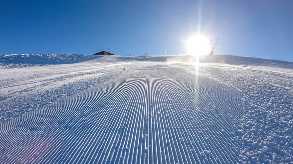 A skier going down the slope in Goldeck, Austria. Perfectly groomed slopes. The crispy snow is thrown up under the pressure of the ski. Man wears green trousers, blue jacket and helm for protection