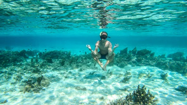 Man in masker and fins snorkelling in a vivid coral reef in Komodo National Park Indonesia. The man is sitting in a meditation pose. Crystal clear water. Air bubbles around him. Under water meditation