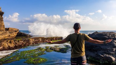 A man standing next to an edge of a cliffs, enjoying the waves splashing on cliffs, next to Tanah Lot Temple, Bali, Indonesia. Power of the nature. The man is enjoying his time and surrounding nature