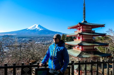 A man admiring Chureito Pagoda and view on Mt Fuji, Japan, captured on a clear, sunny day in winter. Top of the volcano covered with snow. He is enjoying his time, contemplating the beauty of nature
