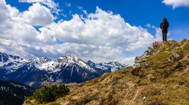 A man with big hiking backpack hiking to Himmeleck peak, Austria. There is a massive mountain range in the back, partially covered with snow. Early spring vibes. Freedom and adventure.