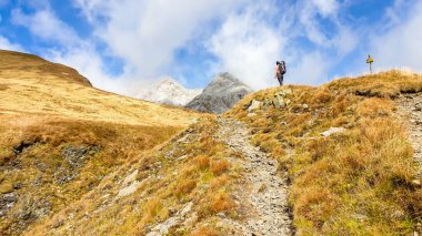 A man with a big backpack hiking through golden colored mountains on the Austrian-Italian border. The man is enjoying the autumn vibes in Alps. Sharp Alpine peaks in the back. Serenity and solitude
