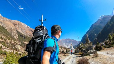 A couple trekking along the barren pathway in Annapurna Circuit in Nepal. They are having fun, enjoying the view. There is a lush green Himalayan valley around. Snow caped mountains in the back.