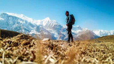 A man trekking on the Annapurna Circuit Trek, Himalayas, Nepal. Snow caped Annapurna chain in the back. Clear weather, dry grass, snowy peaks. High altitude, massive mountains. Freedom and adventure