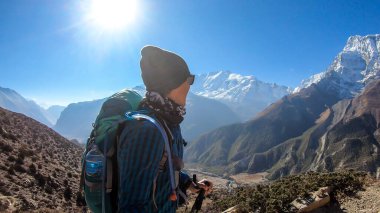 Man taking a selfie while trekking on the Annapurna Circuit Trek, Himalayas, Nepal. Snow caped Annapurna chain in the back. Lots of dried grass. High altitude, massive mountains. Freedom and adventure