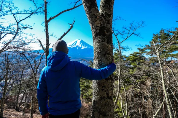 A man standing in a forest on the hilltop above Chureito Pagoda, Japan with Mt Fuji in the back. He is having a lot of fun, enjoying beautiful landscape. Holly mountain in Japan. Clear and sunny day