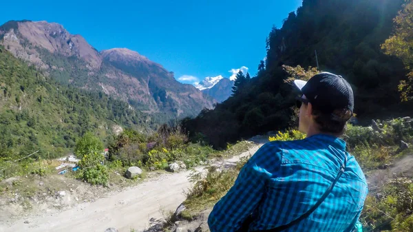 A man in blue shirt enjoying the view on Himalayas on Annapurna Circuit Trek, Nepal. Dense trees. He is taking a break while trekking to soak in the views. Massive mountain ranges. Peace of mind