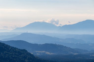 Avusturya, Carinthia 'daki sonsuz dağ zincirlerinin panoramik görüntüsü. Dağlar sisle örtülüdür. Uzakta Piramidenkogel Kulesi 'ni görebilirsiniz. Dinginlik ve sakinlik