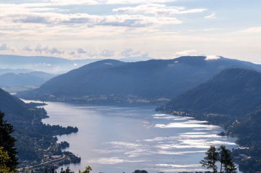 A view on the Lake Ossiach located in the heart of the Alps in Carinthia, Austria. The surface of the lake reflects golden sunbeams. The view is from a chapel on the hilltop of Oswaldiberg. clipart