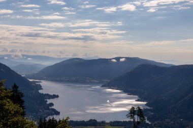 A small swallow flying with the view on the Lake Ossiacher located in between high Alpine peaks in Austria. The surface if the lake reflects golden sunbeams A bit of overcast. Freedom and calmness clipart