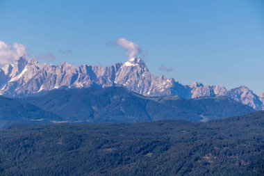 A close up view on Dobratsch, a mountain in Austrian Alps. The mountain's sides are baren and sharp. High mountaineering. Clear and blue sky, with a few clouds above the peaks. Calmness.