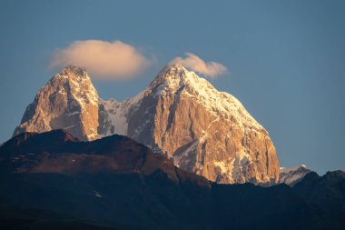 Gürcistan, Kafkasya 'daki Ushba tepelerine ulaşan ilk gün doğumu. Yüksek ve karlı dağların üzerindeki bulutsuz gökyüzü. Aşağıdaki tepeler gölgelerle kaplı. Şafak. Yüksek ve ıssız dağlar