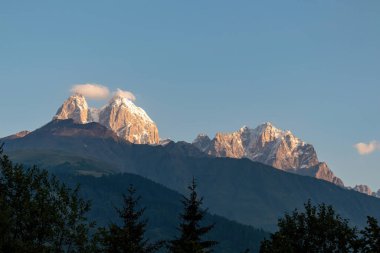 Gürcistan, Kafkasya 'daki Ushba tepelerine ulaşan ilk gün doğumu. Yüksek ve karlı dağların üzerindeki bulutsuz gökyüzü. Aşağıdaki tepeler gölgelerle kaplı. Şafak. Yüksek ve ıssız dağlar
