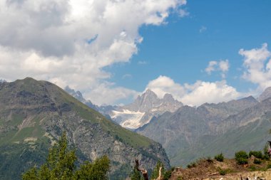 A panoramic view on high Caucasus mountains in Georgia. There are high, snowcapped peaks in the back. Thick clouds above the peaks. Idyllic landscape. Calmness and meditation. Natural remedy clipart