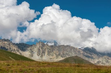 Gürcistan 'daki yüksek Kafkasya dağlarında panoramik bir manzara. Arkada yüksek buzullar var. Keskin tepelerin üzerindeki kalın bulutlar. Kenarları yemyeşil. Çorak tepeler. Idyllic manzara.