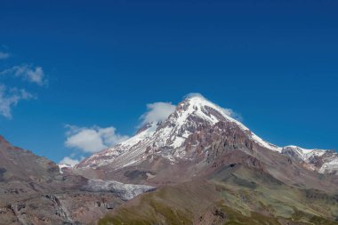 Kafkasya, Georgia 'daki Kazbeg Dağı' nın bulutsuz manzarası. Orada kar kaplı tepenin ve Gergeti Buzulu 'nun altında çorak ve taşlı yamaçlar var. Sükunet. Doğal bir ilaç. Devasa buzul ayağı.