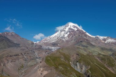 Kafkasya, Georgia 'daki Kazbeg Dağı' nın bulutsuz manzarası. Orada kar kaplı tepenin ve Gergeti Buzulu 'nun altında çorak ve taşlı yamaçlar var. Sükunet. Doğal bir ilaç. Devasa buzul ayağı.