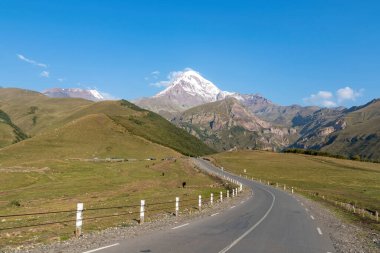 Kafkasya, Georgia 'daki Kazbeg Dağı' nın bulutsuz manzarası. Karla kaplı tepenin altında yemyeşil otlaklar ve yeşil tepeler var ve Gergeti Buzulu. Huzur ve sükunet. Doğal tedavi..