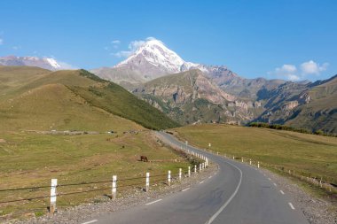 Kafkasya, Georgia 'daki Kazbeg Dağı' nın bulutsuz manzarası. Karla kaplı tepenin altında yemyeşil otlaklar ve yeşil tepeler var ve Gergeti Buzulu. Huzur ve sükunet. Doğal tedavi..
