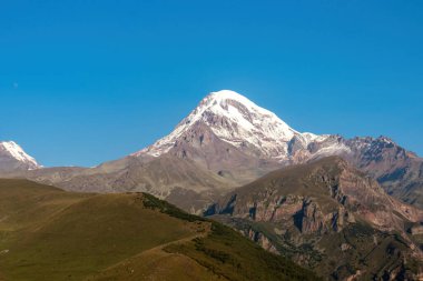 Kafkasya, Georgia 'daki Kazbeg Dağı' nın bulutsuz manzarası. Orada kar kaplı tepenin ve Gergeti Buzulu 'nun altında çorak ve taşlı yamaçlar var. Sükunet. Doğal bir ilaç. Devasa buzul ayağı.