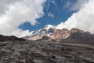 Kafkasya, Georgia 'daki Kazbeg Dağı' nın bulutsuz manzarası. Orada kar kaplı tepenin ve Gergeti Buzulu 'nun altında çorak ve taşlı yamaçlar var. Sükunet. Doğal bir ilaç. Devasa buzul ayağı.