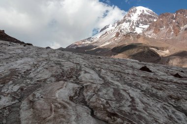 Kafkasya, Georgia 'daki Kazbeg Dağı' nın bulutsuz manzarası. Orada kar kaplı tepenin ve Gergeti Buzulu 'nun altında çorak ve taşlı yamaçlar var. Sükunet. Doğal bir ilaç. Devasa buzul ayağı.