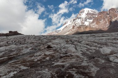 Kafkasya, Georgia 'daki Kazbeg Dağı' nın bulutsuz manzarası. Orada kar kaplı tepenin ve Gergeti Buzulu 'nun altında çorak ve taşlı yamaçlar var. Sükunet. Doğal bir ilaç. Devasa buzul ayağı.