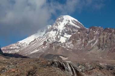 Kafkasya, Georgia 'daki Kazbeg Dağı' nın bulutsuz manzarası. Orada kar kaplı tepenin ve Gergeti Buzulu 'nun altında çorak ve taşlı yamaçlar var. Sükunet. Doğal bir ilaç. Devasa buzul ayağı.