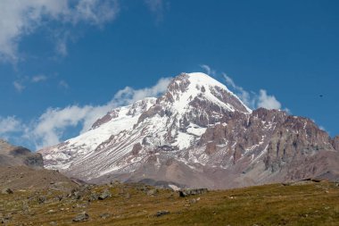 Kafkasya, Georgia 'daki Kazbeg Dağı' nın bulutsuz manzarası. Orada kar kaplı tepenin ve Gergeti Buzulu 'nun altında çorak ve taşlı yamaçlar var. Sükunet. Doğal bir ilaç. Devasa buzul ayağı.
