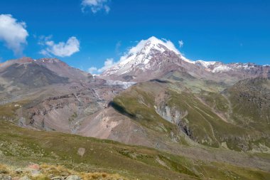 Kafkasya, Georgia 'daki Kazbeg Dağı' nın bulutsuz manzarası. Orada kar kaplı tepenin ve Gergeti Buzulu 'nun altında çorak ve taşlı yamaçlar var. Sükunet. Doğal bir ilaç. Devasa buzul ayağı.