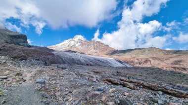 Kafkasya, Georgia 'daki Kazbeg Dağı' nın bulutsuz manzarası. Orada kar kaplı tepenin ve Gergeti Buzulu 'nun altında çorak ve taşlı yamaçlar var. Sükunet. Doğal bir ilaç. Devasa buzul ayağı.