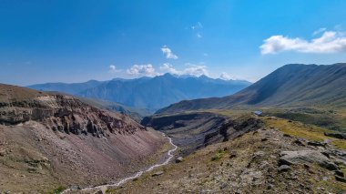 Georgia, Kafkasya 'da bir vadide akan bulutsuz bir nehir manzarası. Orada kar kaplı tepenin ve Gergeti Buzulu 'nun altında çorak ve taşlı yamaçlar var. Sükunet. Doğal tedavi.