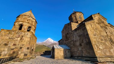 Gürcistan, Stepansminda 'daki Gergeti Trinity Kilisesi' ne yakından bakın. Kilise yüksek bir Kafkas dağında yer almaktadır. Kilisenin üstündeki açık ve mavi gökyüzü. Arkadaki kar kaplı Kazbek Dağı.