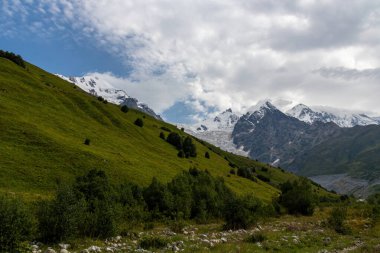 Gürcistan 'ın Büyük Kafkasya Dağları' ndaki Tetnuldi, Gistola ve Lakutsia 'nın karlı zirvelerine panoramik bir manzara. Çayırları yemyeşil tepeler, keskin tepeler, yürüyüş titreşimleri....