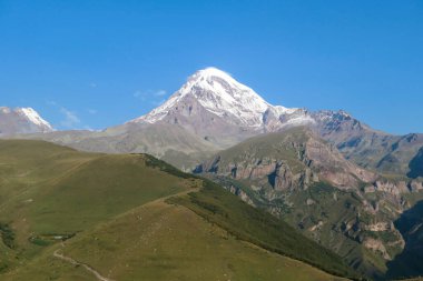 Kafkasya, Georgia 'daki Kazbeg Dağı' nın bulutsuz manzarası. Orada kar kaplı tepenin ve Gergeti Buzulu 'nun altında çorak ve taşlı yamaçlar var. Sükunet. Doğal bir ilaç. Devasa buzul ayağı.
