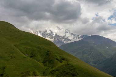 Gürcistan 'ın Büyük Kafkasya Dağları' ndaki Tetnuldi, Gistola ve Lakutsia 'nın karlı zirvelerine panoramik bir manzara. Çayırları yemyeşil tepeler, bulutlarla kaplı tepeler..