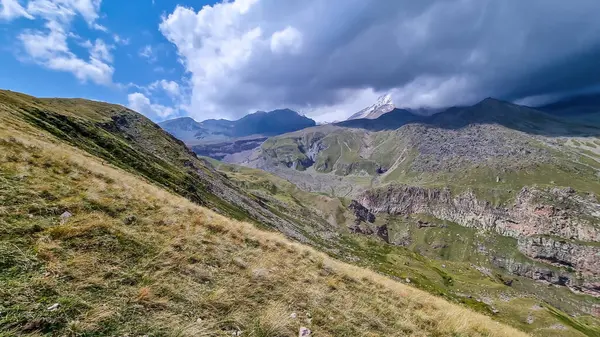 Gürcistan, Kafkasya 'daki Kazbeg Dağı üzerinde güçlü bir bulutlu bina. Yağmurlu bulutlar. Orada kar kaplı tepenin ve Gergeti Buzulu 'nun altında çorak ve taşlı yamaçlar var. Devasa buzul ayağı.