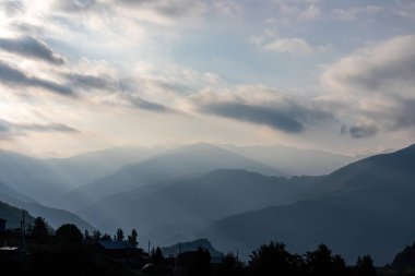 Panoramic view on the mountain chains shrouded in the morning fog after sunrise,seen from village Roshka in the Greater Caucasus Mountain Range in Georgia,Kazbegi Region.Sunrays are touching the peaks clipart