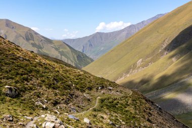 Gürcistan, Kazbegi Bölgesi 'ndeki Büyük Kafkasya Dağları' nda yeşil tepeler ve dağ tepeleri üzerinde panoramik manzaralı bir yürüyüş yolu. Seyahat tutkusu. Temiz Gökyüzü. Koşun!