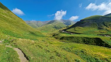 A hiking trail leading through a vast green grassland in the Greater Caucasus Mountain Range in Georgia, Kazbegi Region. The surrounding mountains and hills are green and soft. Tranquility. Highlands clipart