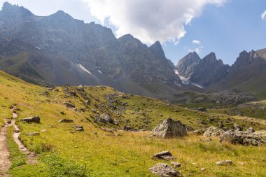 Gürcistan, Kazbegi Bölgesi 'ndeki Büyük Kafkasya Dağları' ndaki Chaukhi topluluğunun keskin dağ zirvelerine panoramik bir manzara. Yeşil bir çayırda yürüyüş parkuru. Gürcü Dolomitler.
